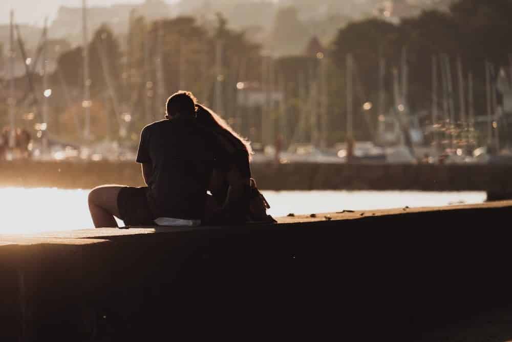 couple sitting on a dock with their arms around each other letting their guard down